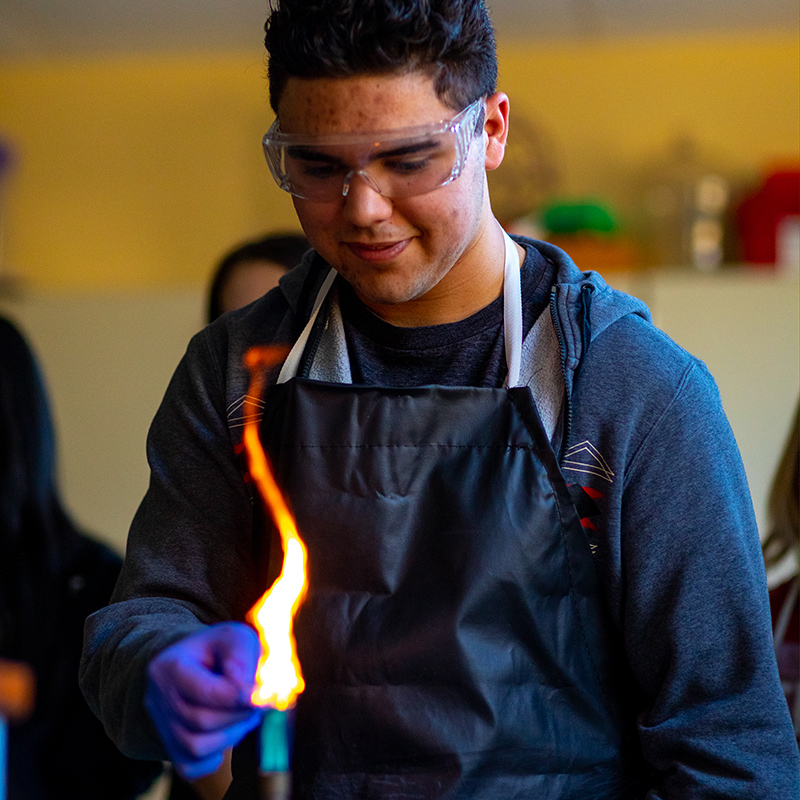 student in science lab with flame and safety goggles