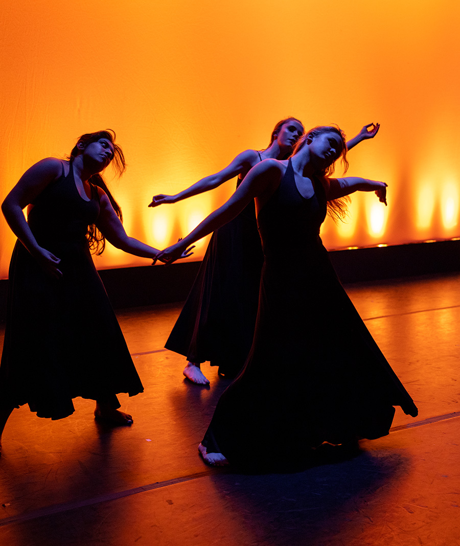 dancers in black dresses on orange lit stage
